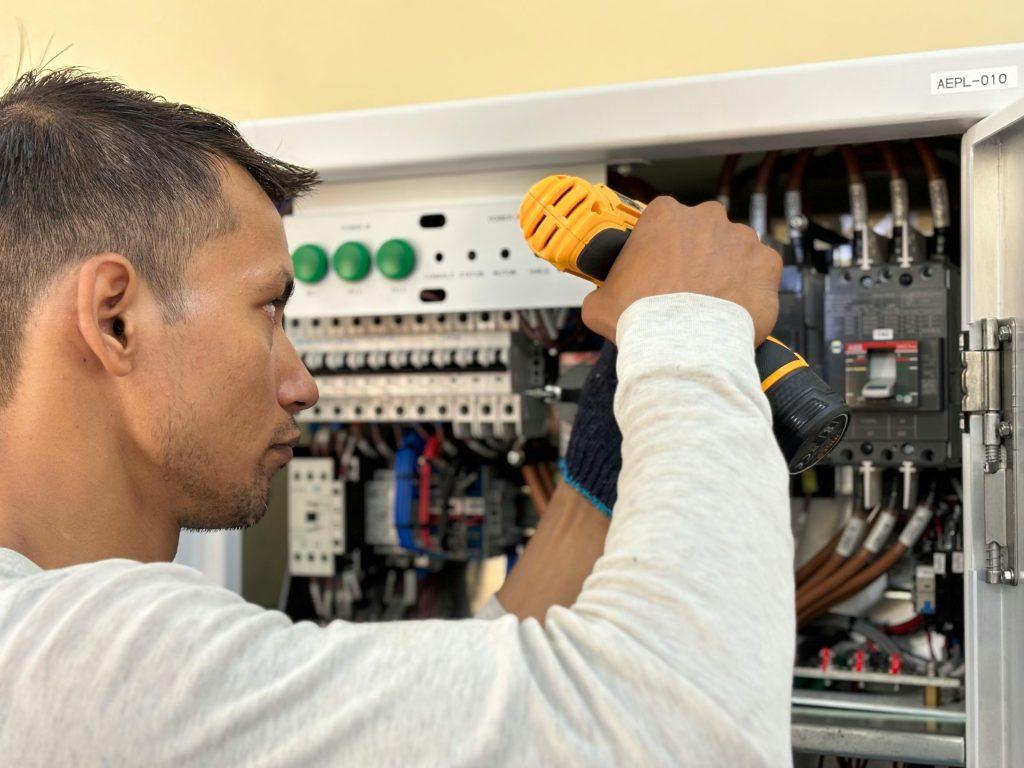 An electrician with an electric screwdriver repairs an electric panel. 