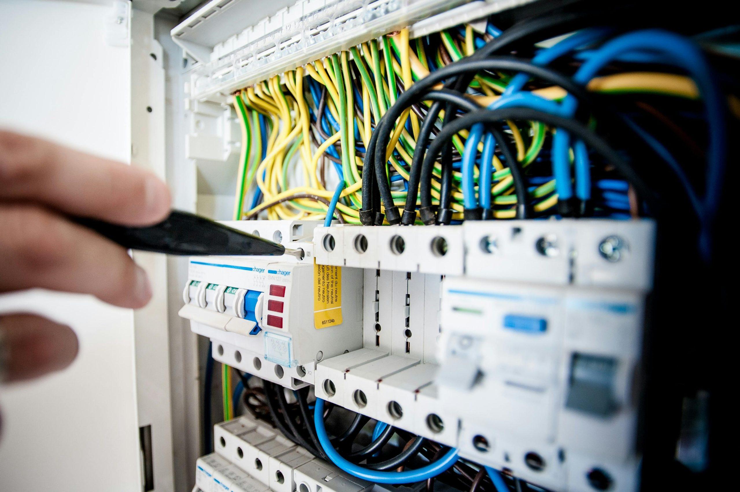 An electrician's hand repairs wires and components of an electrical panel. - Visit phaselectric.com.