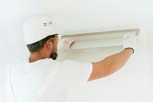 Electrician in white t-shirt and white hard hat installing light panel.